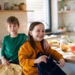 Little children packing to school in morning in kitchen.
