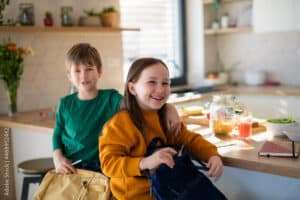 Little children packing to school in morning in kitchen.