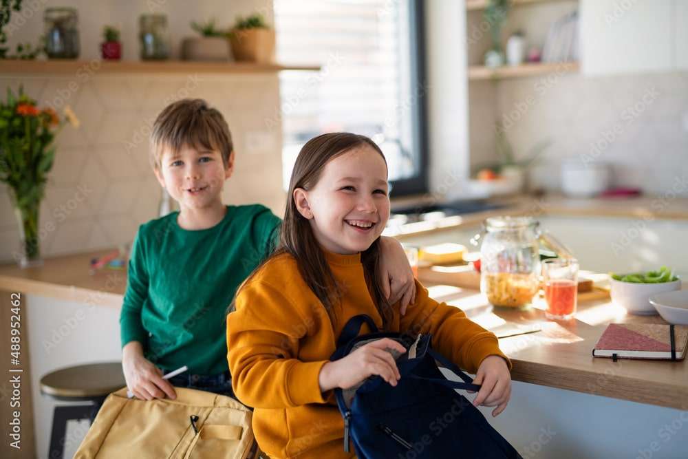Little children packing to school in morning in kitchen.