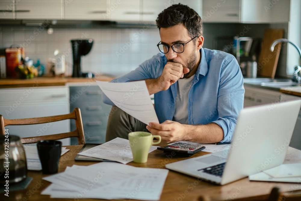 Worried young Caucasian man going over his bills and home finances in the morning in the kitchen