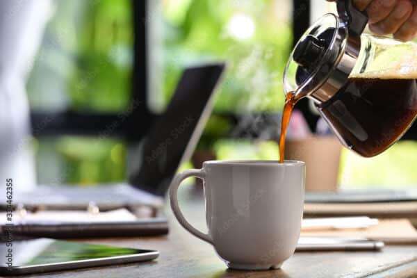 A hand pouring steaming coffee in to a cup on a work desk when work from home